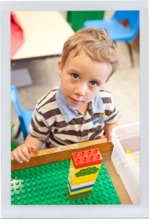 Photograph: A preschool-aged boy looks up from his stack of building blocks. (Photograph by Alex Lazara)